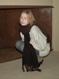 Woman in a light grey sweatshirt and dark brown scarf, crouched down.