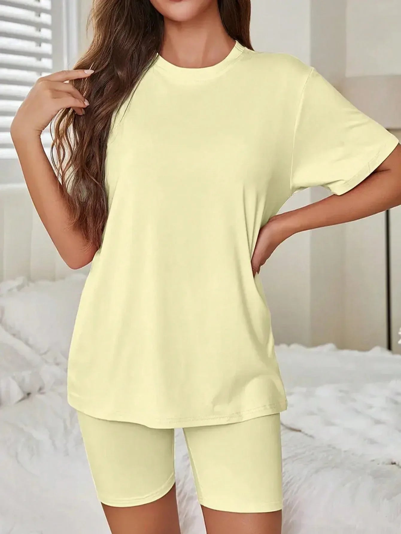 Front view of a woman in a pale yellow short sleeve t-shirt and bike shorts set, posing with hands on hips.
