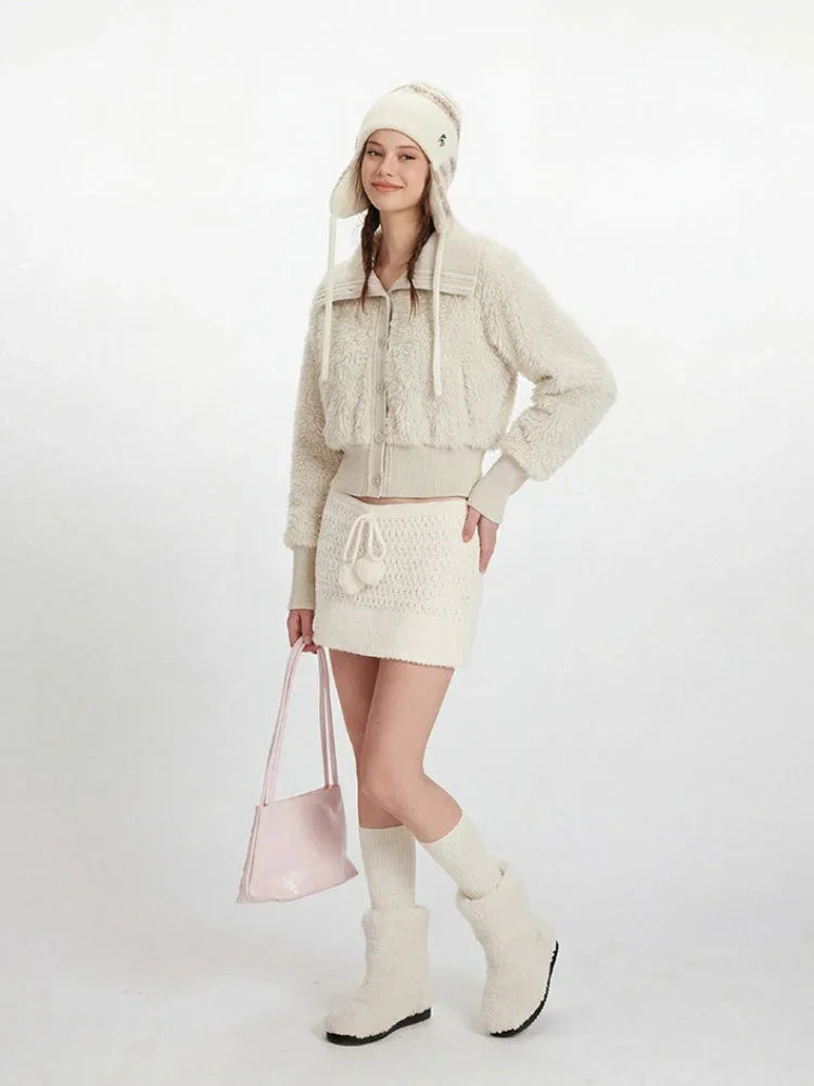Woman wearing a cream fuzzy cropped jacket and matching mini skirt, with a knitted hat and boots