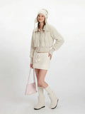 Front view of a woman in a cream fuzzy cropped jacket, white knit mini skirt, and matching accessories