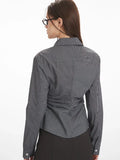 Rear view of a woman wearing a grey textured long-sleeve collared shirt with ruched waist detailing and a black midi skirt.