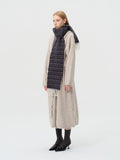 Side profile of a woman wearing a dark stripe scarf with fringed ends over a beige cardigan.