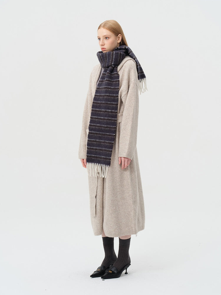 Side profile of a woman wearing a dark stripe scarf with fringed ends over a beige cardigan.