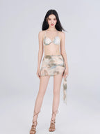 Woman wearing a bikini top and a sheer abstract print ruched skirt, styled with strappy sandals.