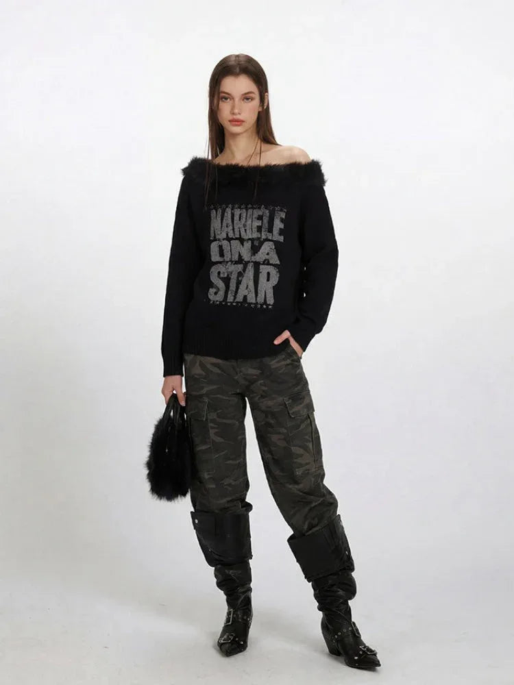 Full body shot of a woman modeling a black off-the-shoulder graphic print sweater with faux fur trim, styled with cargo pants.