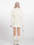 Rear view of a woman wearing a cream knit turtleneck sweater with puffed sleeves over a cream knit mini skirt with a drawstring waist.