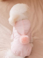 Rear view of a Bichon Frise dog wearing a pink gingham hooded dog suit with a pink pom-pom accent.