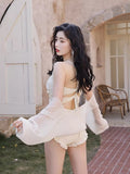 Rear view of a woman in a white lace swimsuit showing the back strap detail and sheer cover-up.