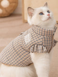 Close-up of a cat wearing a brown plaid pet vest, highlighting the collar and ruffled sleeves.