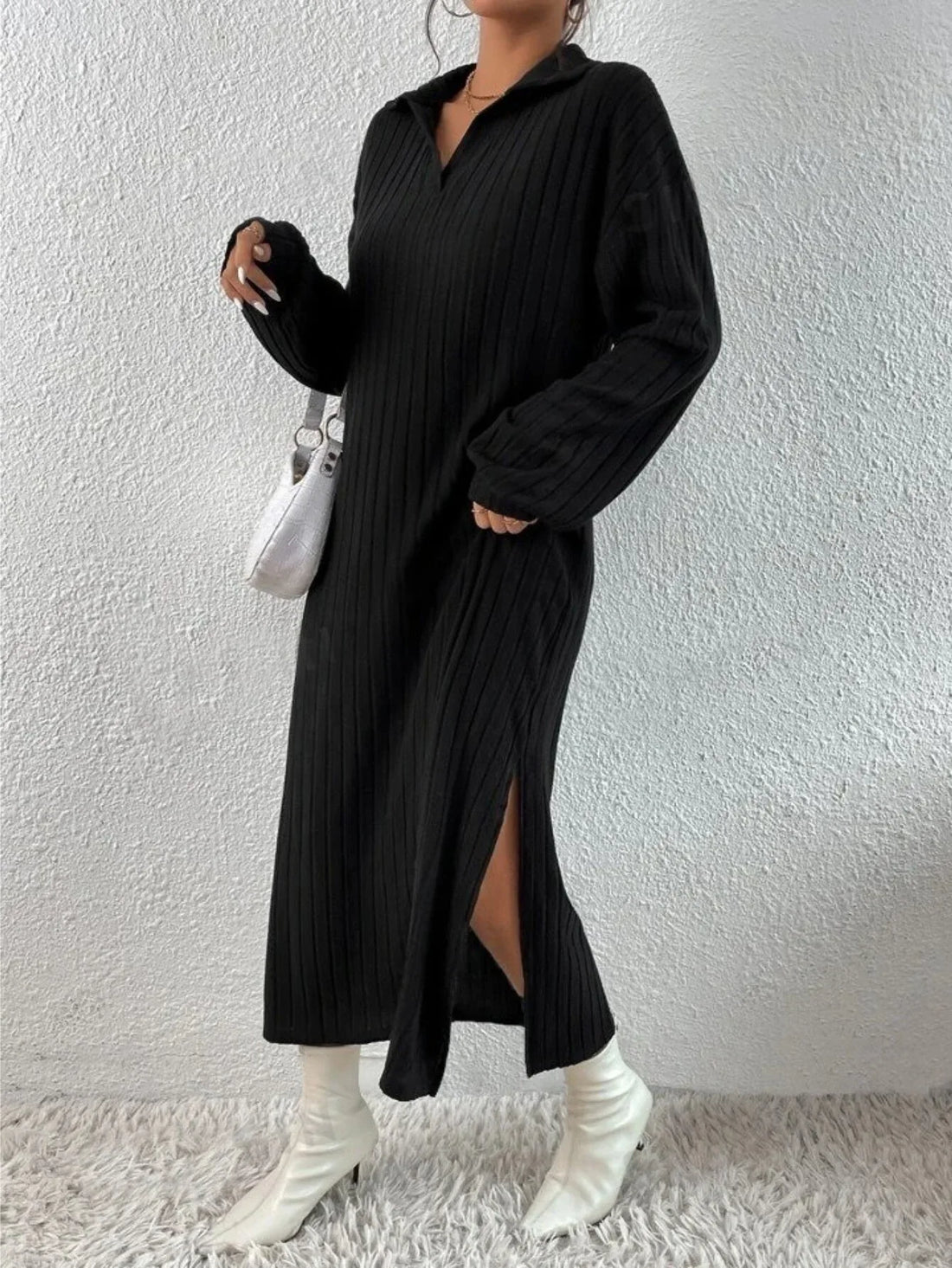 Model wearing a black ribbed knit midi dress with a pointed collar and v-neck, featuring long sleeves and a side slit.