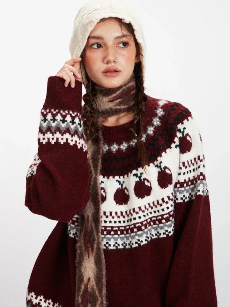 Model posing in a burgundy Fair Isle sweater with apple design, styled with a scarf and hat