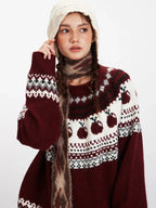 Model posing in a burgundy Fair Isle sweater with apple design, styled with a scarf and hat