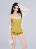 Woman wearing a mustard yellow one-piece swimsuit with floral trim and ruffled shorts, paired with a sheer white cover-up.