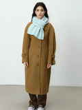 Full body shot of a woman wearing a camel coat and light blue scarf