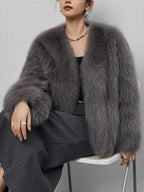 Woman sitting down wearing a grey faux fur jacket and dark trousers.