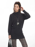 Side profile of a woman wearing a charcoal grey knit turtleneck tunic sweater and a star pendant necklace.