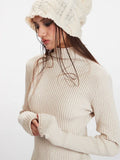 Close-up of a woman wearing a cream ribbed knit turtleneck sweater with fingerless gloves and a cream textured knit beanie.