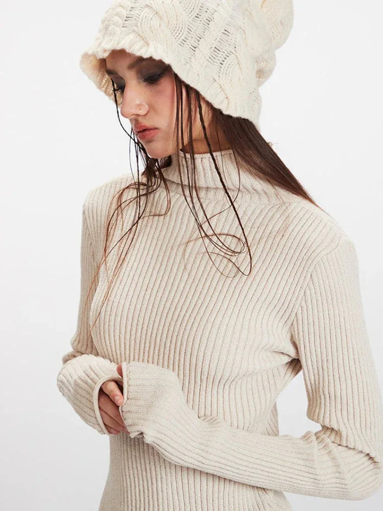 Close-up of a woman wearing a cream ribbed knit turtleneck sweater with fingerless gloves and a cream textured knit beanie.