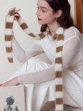 Close-up of a woman wearing a white long-sleeved top and white pants, with a brown and white striped fuzzy scarf draped around her neck.