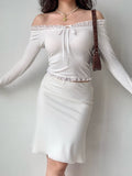 woman wearing a white off-the-shoulder ribbed knit top with lace trim and a tie closure at the neckline, paired with a white skirt