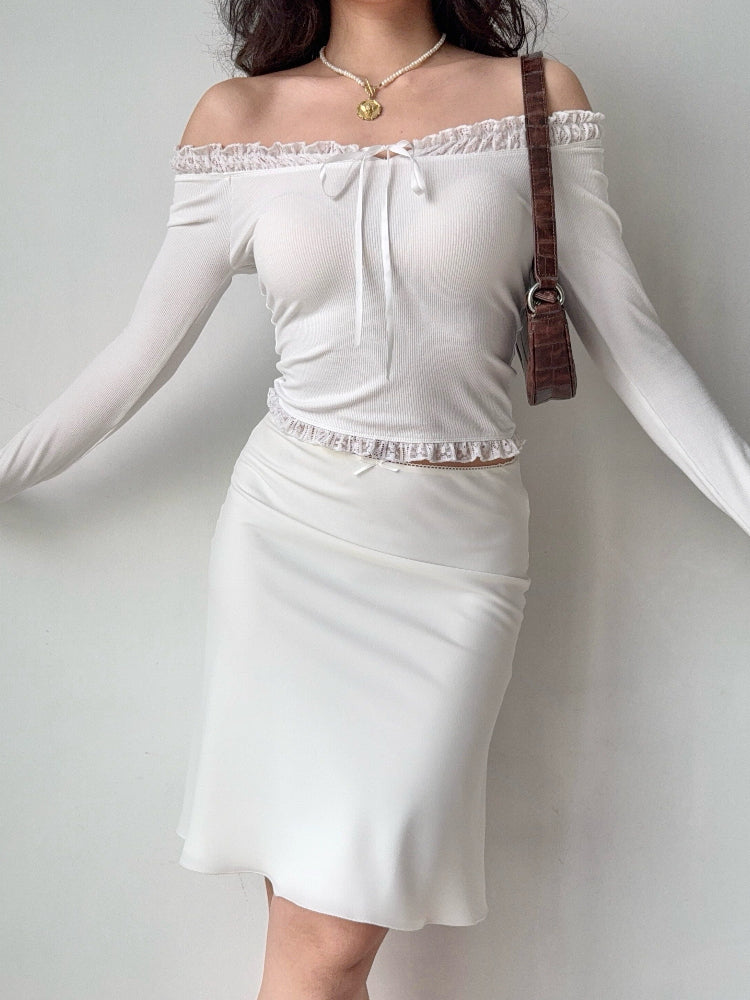 woman wearing a white off-the-shoulder ribbed knit top with lace trim and a tie closure at the neckline, paired with a white skirt