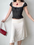 Full body shot of a woman in a black polka dot top and white asymmetrical skirt, holding a red handbag