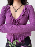 Close-up of a woman wearing a purple textured mesh long-sleeve top with a tie-front closure and ruffled V-neck.
