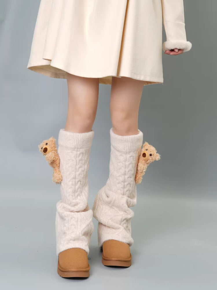 Cream cable knit leg warmers with teddy bear embellishments and pom-poms, worn with a cream dress and tan boots.