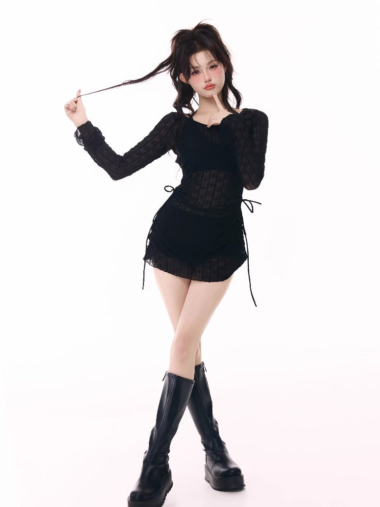 Woman posing in a black sheer long-sleeve top over a black bikini top and black ruffled hem shorts, with black platform boots.