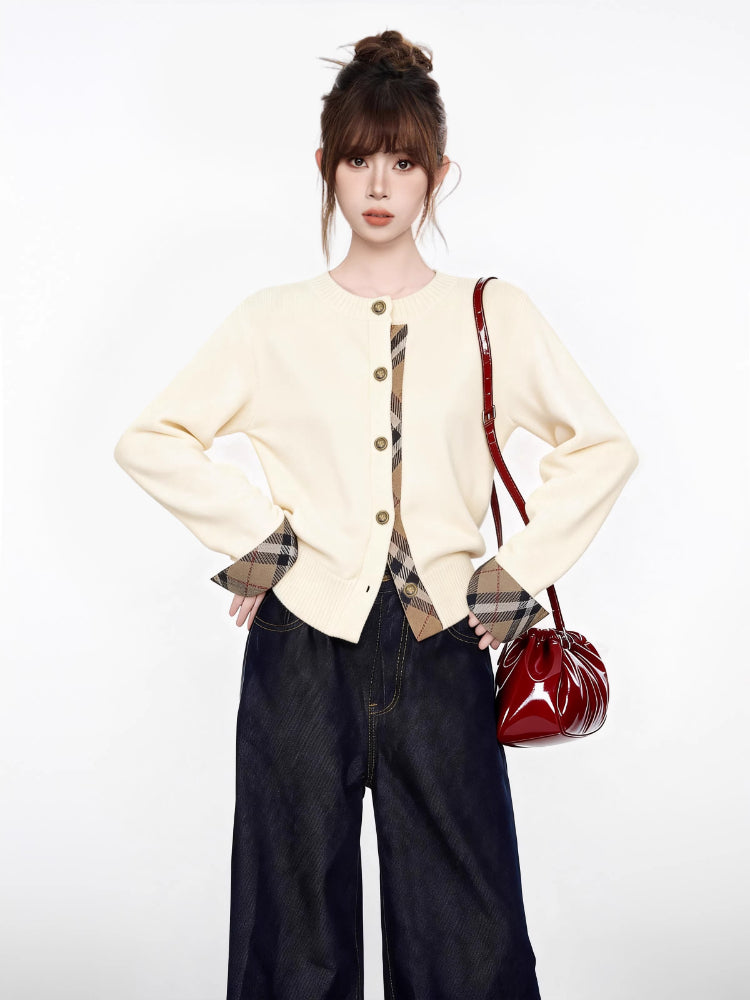 Woman in a cream cardigan with plaid accents, dark wide-leg jeans, and a red handbag.
