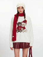 Model posing in a cream fuzzy knit sweater with a festive teddy bear design