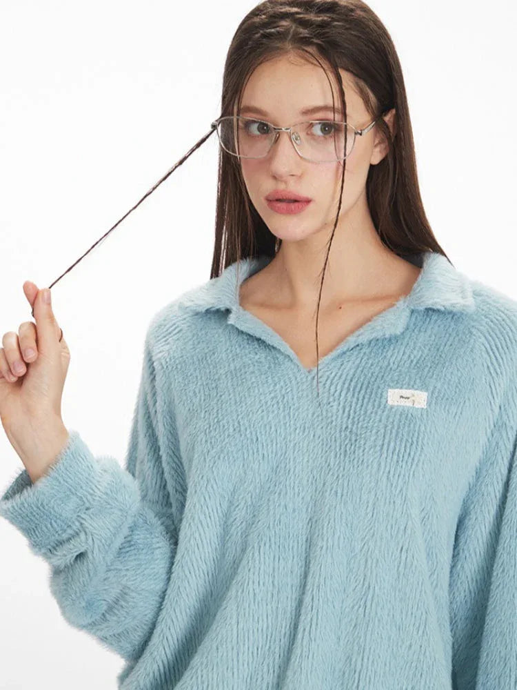 Close-up of a model wearing a light blue fuzzy knit collared v-neck sweater, showing the textured fabric and a small logo patch on the chest.