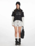Model wearing a black and white long sleeve graphic t-shirt with silver ruffled shorts.