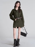 Woman in an olive green dress and black boots, holding sunglasses and a handbag.