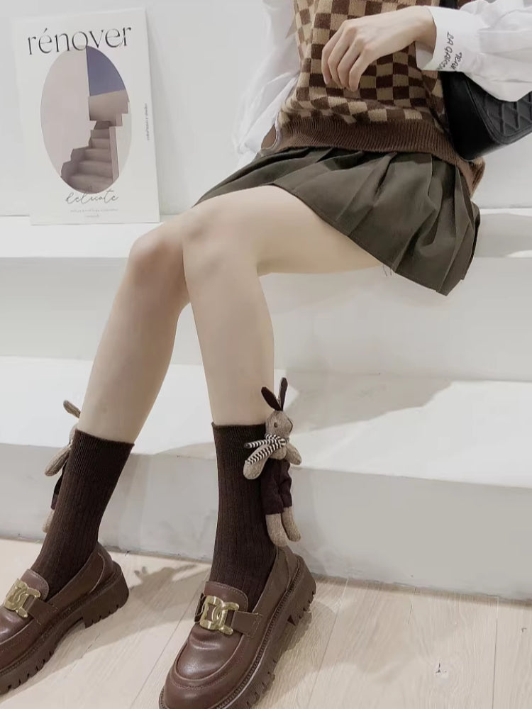 Woman sitting on steps wearing brown crew socks with a 3D bunny embellishment and loafers.