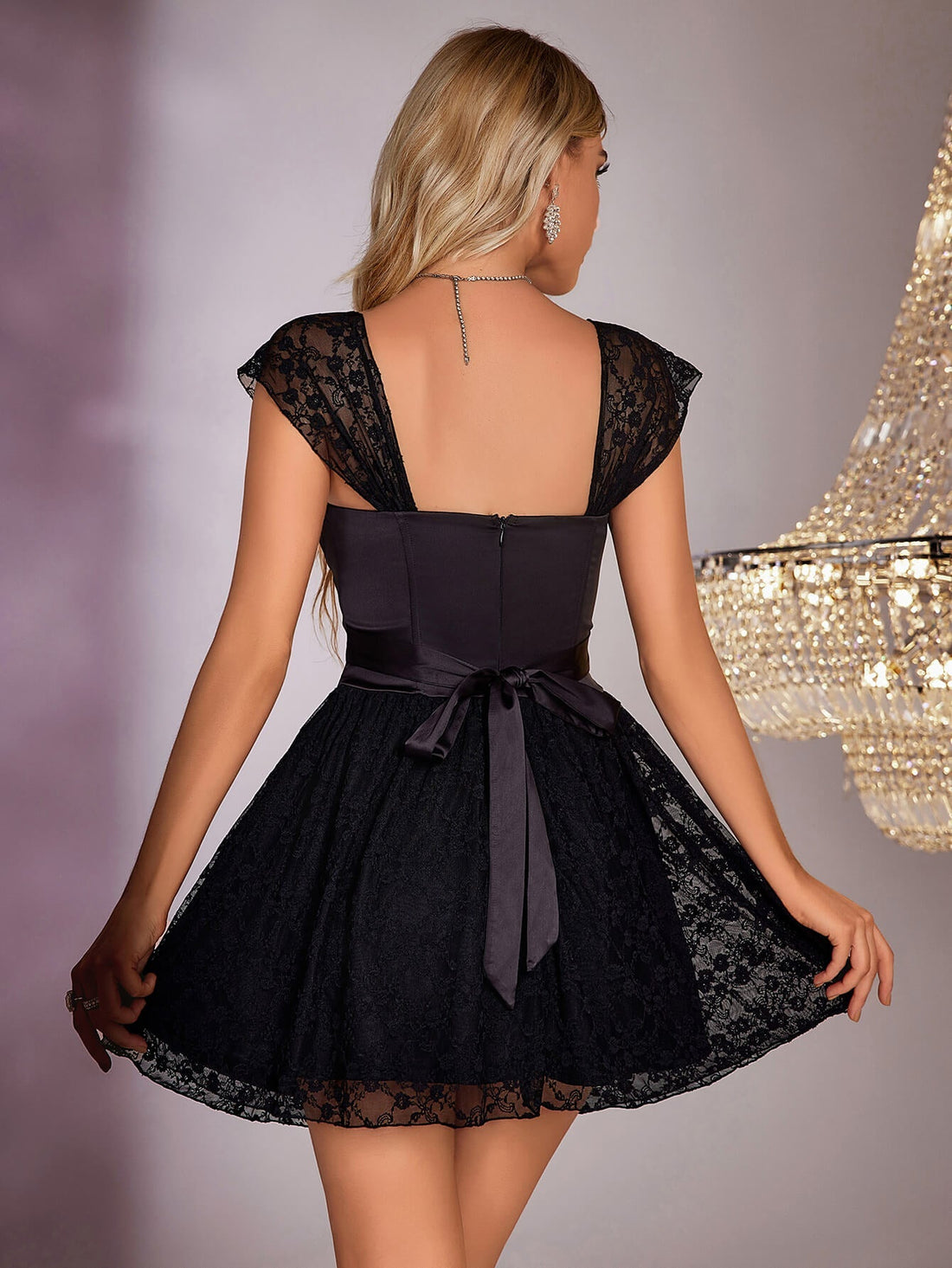 Woman in a black satin and lace A-line dress with sweetheart neckline and cap sleeves, standing in front of a chandelier.