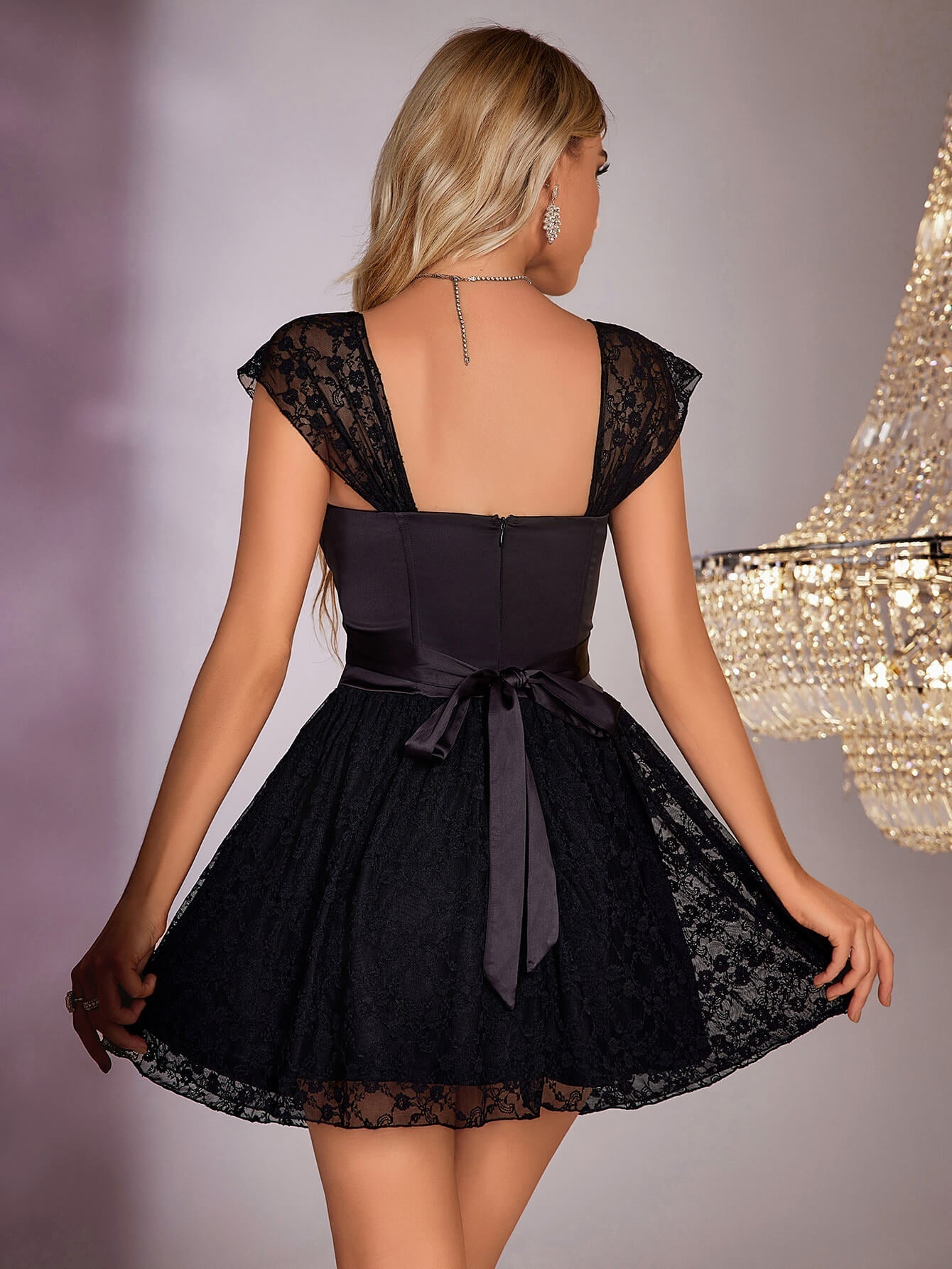 Back view of a woman in a black satin and lace A-line dress, showing the zipper closure and bow detail.