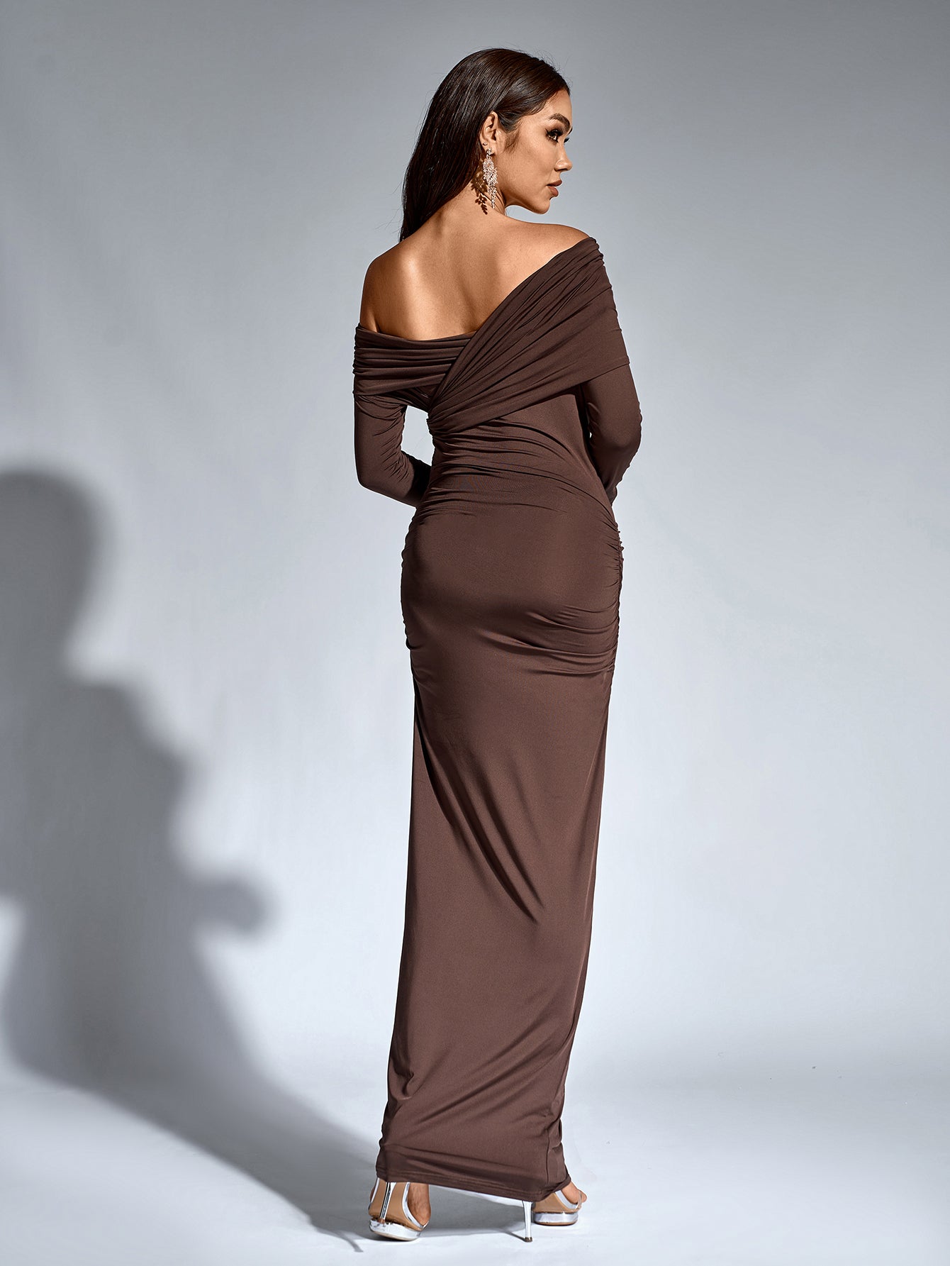 Back view of a woman in a brown long-sleeve one-shoulder draped maxi dress