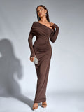 Woman posing with a clutch in a brown long-sleeve one-shoulder draped maxi dress