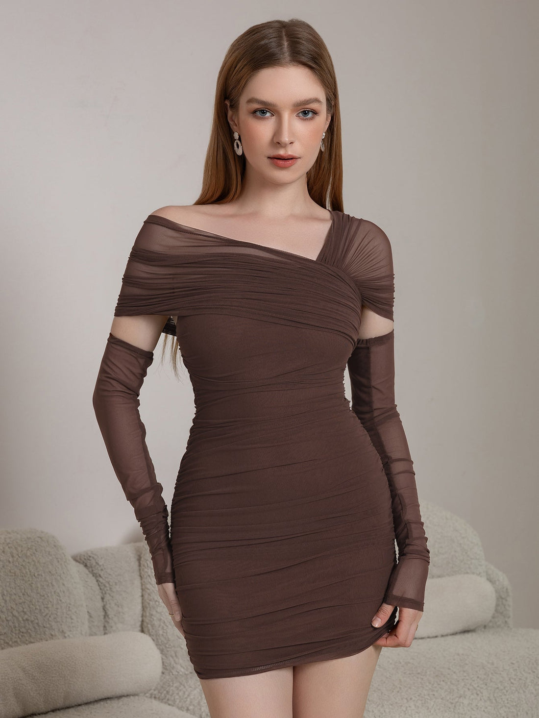 Woman wearing a brown ruched mesh bodycon dress with an asymmetrical neckline and long sleeves with cut-outs.