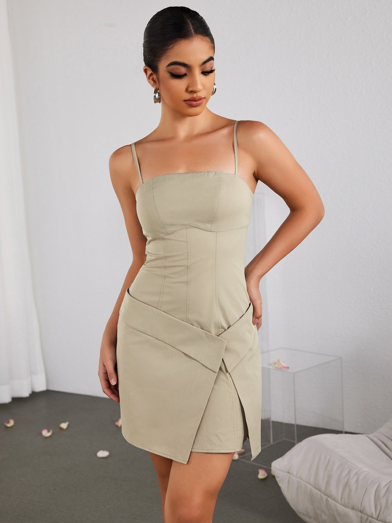 Woman in a beige dress with hands on hips, looking down