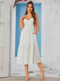 Woman in a black crepe sheath dress with a sweetheart neckline and spaghetti straps, standing with hands in pockets.