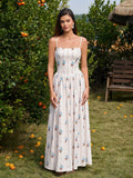 Woman wearing a white floral print maxi dress with spaghetti straps and a square neckline, standing in an orchard.