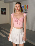 Full body shot of a woman wearing a pink lace-trimmed crop top with a bow detail and a white pleated mini skirt, looking forward.