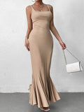 Woman holding a white quilted handbag while wearing a beige maxi dress with a fishtail hem