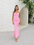 Woman wearing a pink ruched maxi dress with spaghetti straps and a cowl neckline