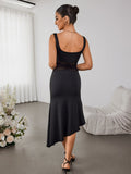 Rear view of a woman in a black sleeveless dress with an asymmetrical hemline and sheer mesh waist detail.