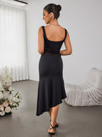 Rear view of a woman in a black sleeveless dress with an asymmetrical hemline and sheer mesh waist detail.