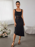 Full body shot of a woman in an elegant black dress with a square neckline and a flowing asymmetrical skirt.