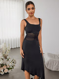 Front view of a woman modeling a black dress with a square neckline and sheer mesh waist detail, showcasing the asymmetrical hem.
